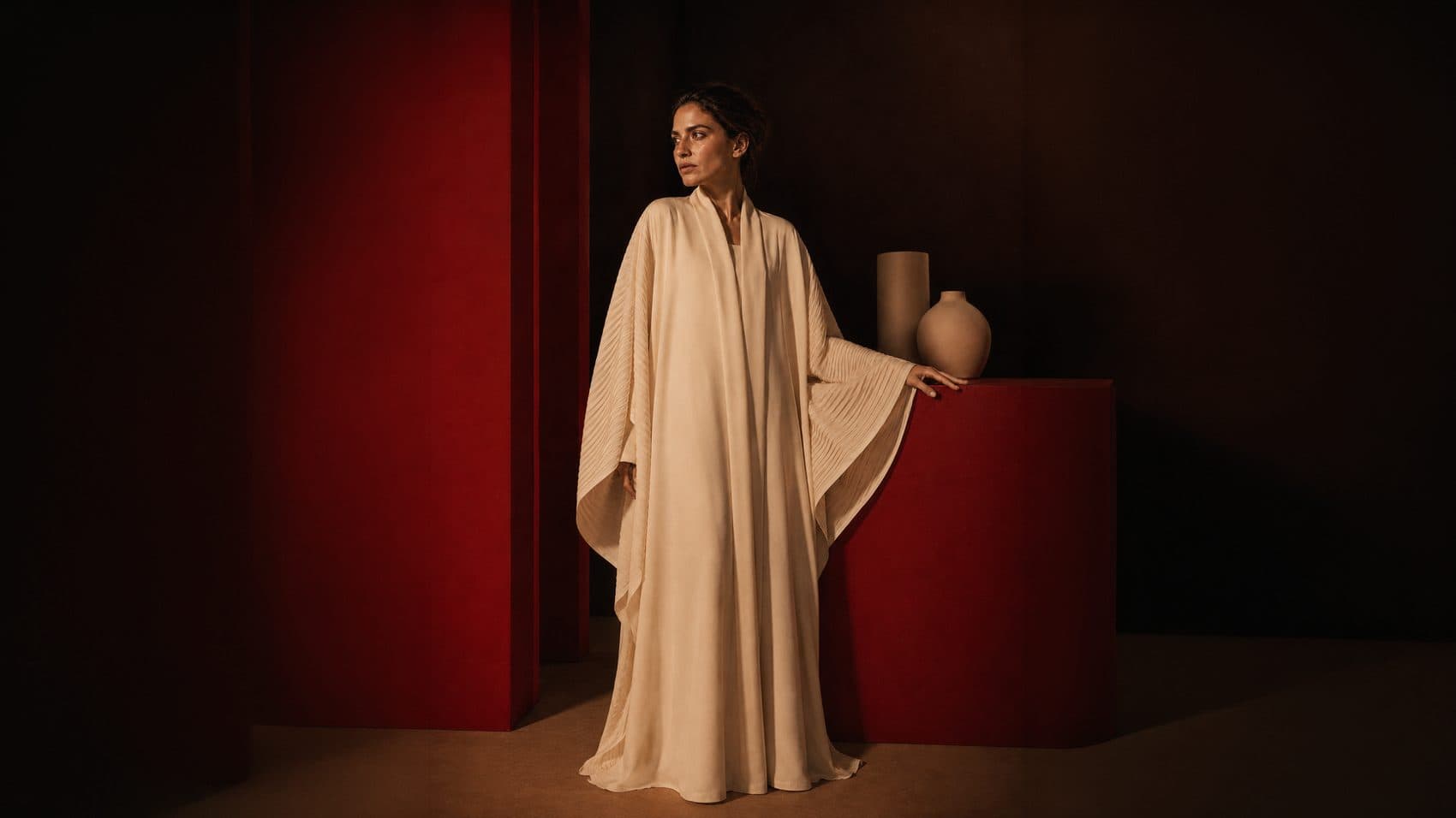 Rawda Autumn/Winter 2024 campaign — a cream pleated abaya against oxblood architecture